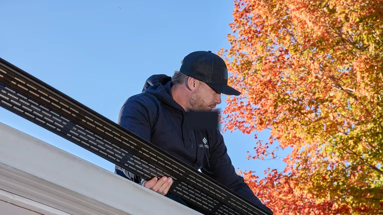 Technician fitting a perforated Alu-Rex gutter guard into a white gutter